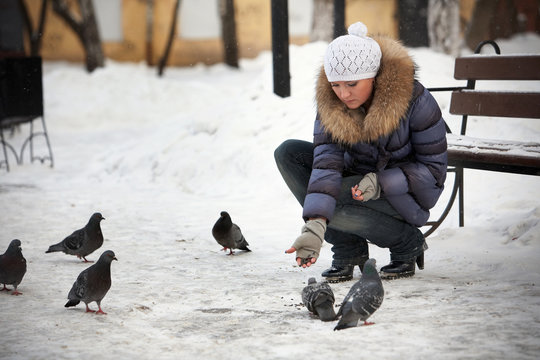 outdoor portrait of a young woman feeding pidgins in a park