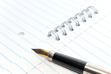A gold nibbed pen on a spiral-bound notepad