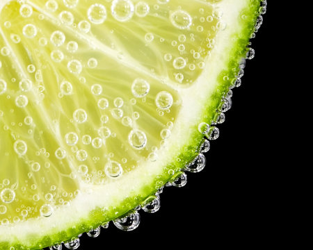 Close-up of a lime slice with bubbles on a black background
