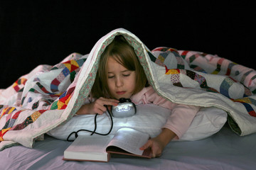 girl reading in bed with a book light