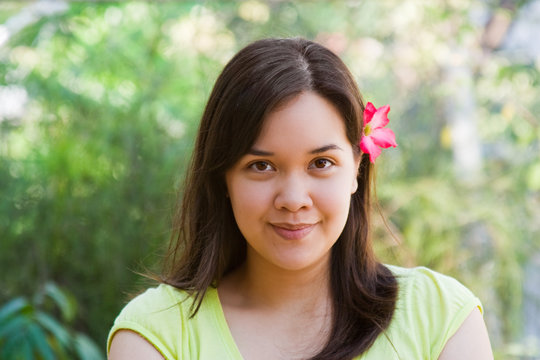 Smiling woman with pink plumeria tucked behind ear