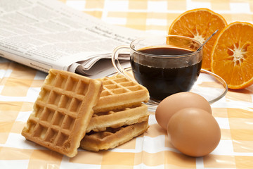 breakfast with cup of coffee, waffles, eggs, orange and newspape