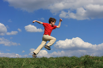 Boy jumping, running against blue sky