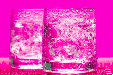 Glass with water and ice over pink