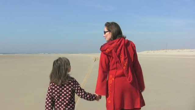 m&egrave;re et fille sur la plage main dans la main de dos