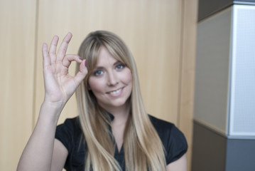 junge blonde frau macht ok zeichen mit hand und lacht