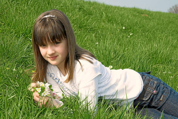 Fototapeta premium Mädchen liegt im Gras mit Blumen in der Hand
