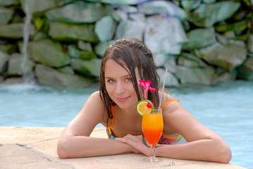 Beautiful young woman by the swimming pool with cocktail