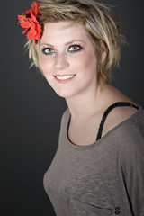 Naklejka premium Shot of a Smiling Blonde Girl with Red Flower in her Hair