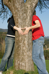 Couple hugging  tree and making a heart.