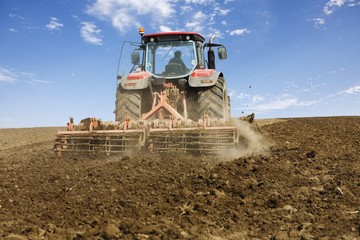 Red tractor working the field, shot from behind