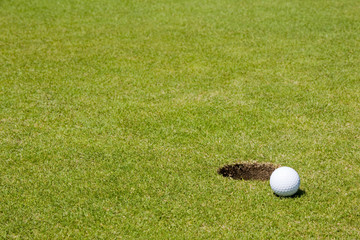 Golf ball very close to a hole on a putting green.