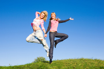 Two happy girls jumping on green meadow.