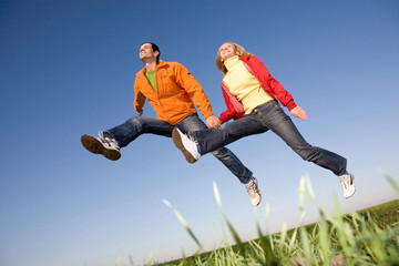 Happy smiling couple  jumping in sky above a green meadow