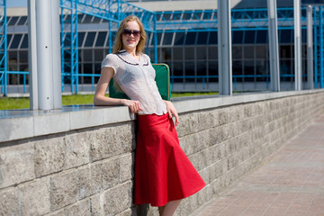 Fototapeta premium Smiling sexy blonde girl wearing red skirt. Near green bag.