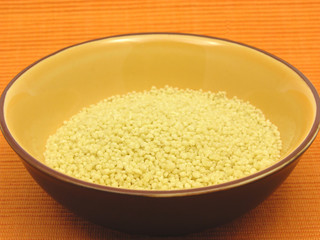 Couscous in einer orangen Keramikschale auf orangem Hintergrund