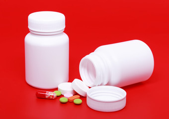 White medicine bottles, colour  pills on red background.