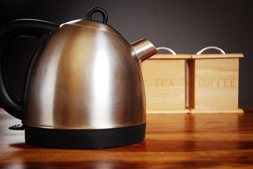 Kettle and mug on dark background with tea and coffee cannisters