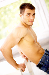 Fototapeta na wymiar Muscular and tanned male is exercising, wearing jeans
