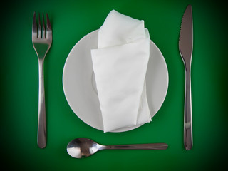 Fork, knife, spoon, plate, and silk napkin on green   background