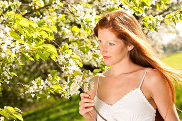 Long red hair woman standing under blooming tree