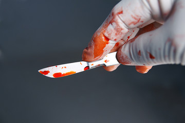 Gloved hand holding scalpel with blood - obrazy, fototapety, plakaty