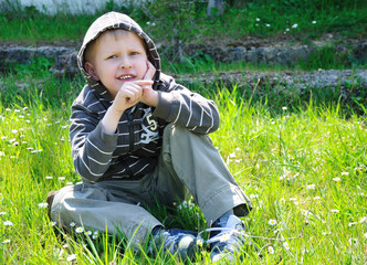 boy sits on the  camomile forest  meadow and points right