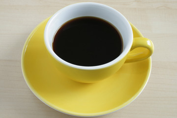 Yellow cup of coffee on wooden table