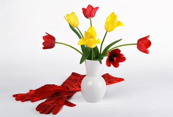 Vase with tulips and red gloves next to it isolated over white