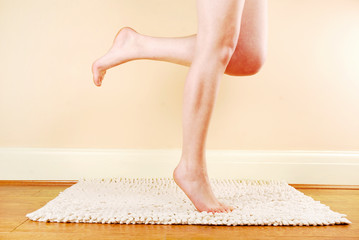 A woman's naked legs standing on a bath mat