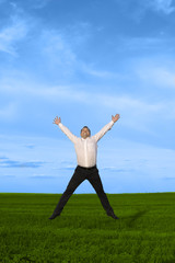 Fototapeta na wymiar Businessman jumping on the green grass over clouds blue sky