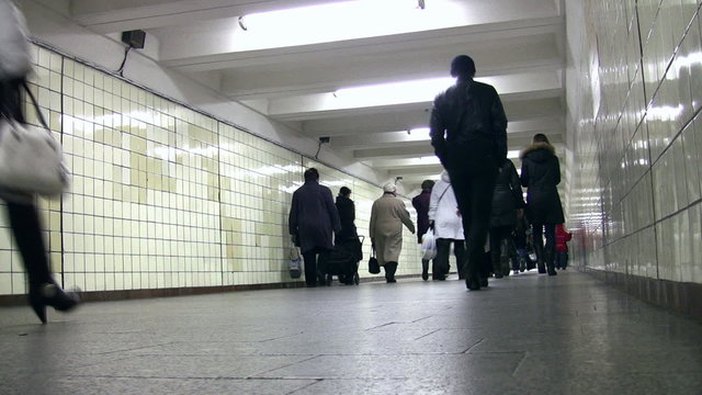 Behind people going in subway corridor. Low view.