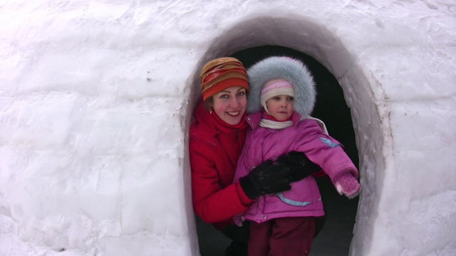 Mother with small girl looks from snow building