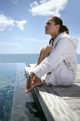 Jeune femme en peignoir assise au bord d'une piscine