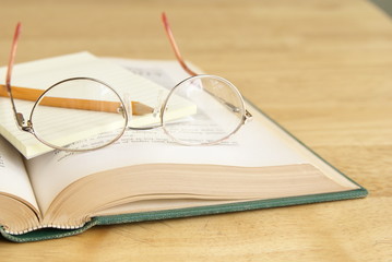 Eyeglasses with pencil and yellow notepad on open book