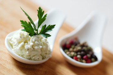 Two spoons with spices and one with cheese with parsley on top