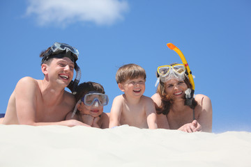 family of four lying on sand with snorkeling masks