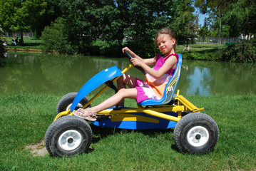 Little girl on the quadrocycle in the border of lake in the park