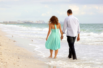 young couple walking hand in hand on the beach thier feet in the