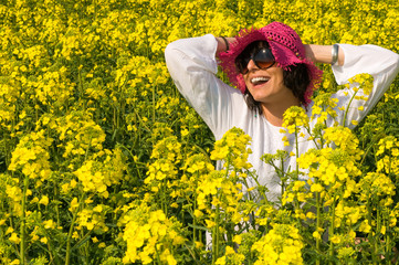 Fototapeta premium Smiling girl in the rapeseed yellow field wearing purple hat