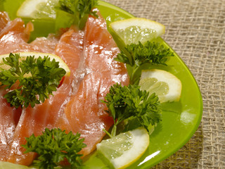 sliced salmon fish on the green plate with greenery and lemon
