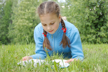 Young beautiful girl lays on green field and reads book