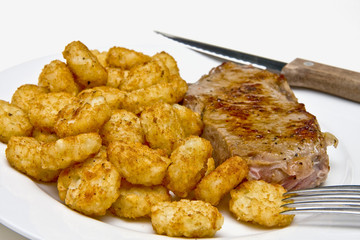 Steak and potato puffs on  white plate