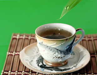 a cup of green tea and a drop of water on a green background