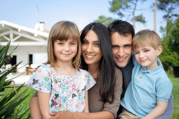 Homme et femme avec enfants souriants devant une maison