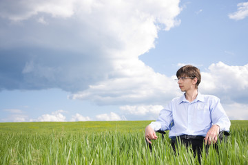 Naklejka na ściany i meble Businessman sitting on grassland under blue sky