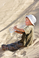 young boy drinking water in sand desert