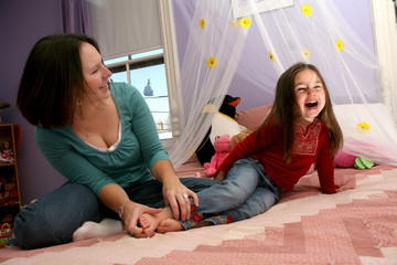 mother tickling her little girl's bare feet on the bed