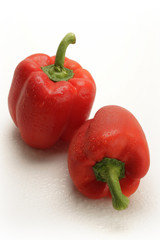 two red peppers with water drops on white background