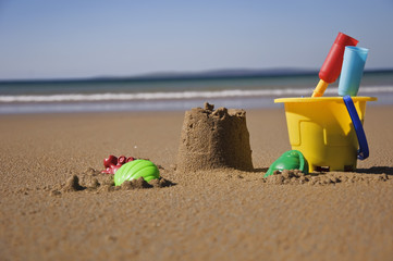 Fototapeta na wymiar childs sand bucket and toys on scenic sunny beach with waves